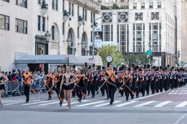 Banda de música desfilando con uniformes naranjas y negros por una calle de la ciudad