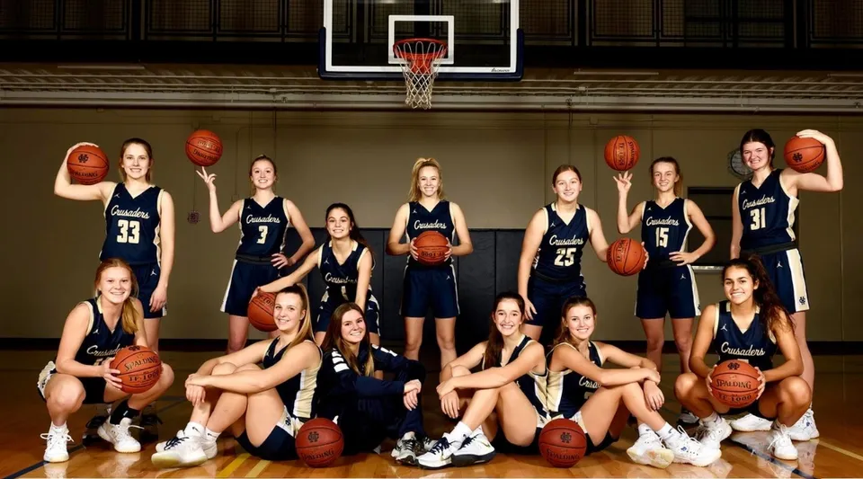 Un gruppo di giocatrici di basket della Bishop Heelan Catholic High School posa insieme nella palestra davanti a un canestro.