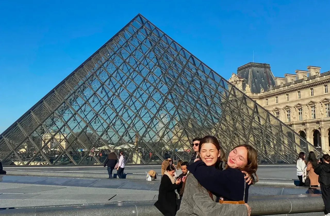 Due studentesse si abbracciano davanti alla piramide di vetro del Louvre a Parigi