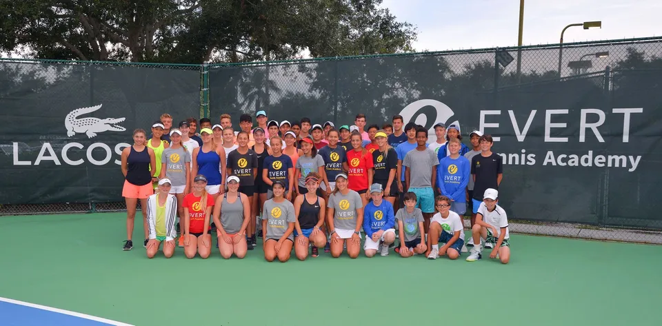 Un grande gruppo di giovani tennisti posa su un campo da tennis della Evert Tennis Academy.