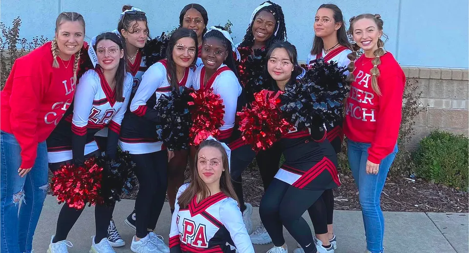 Un gruppo di cheerleader della Life Prep Academy posa davanti a una parete blu con i pompon in mano.