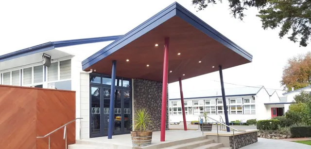 L'edificio moderno a due piani con tettoia rossa e blu nel campus della Hastings Girls' High School è circondato da alberi.