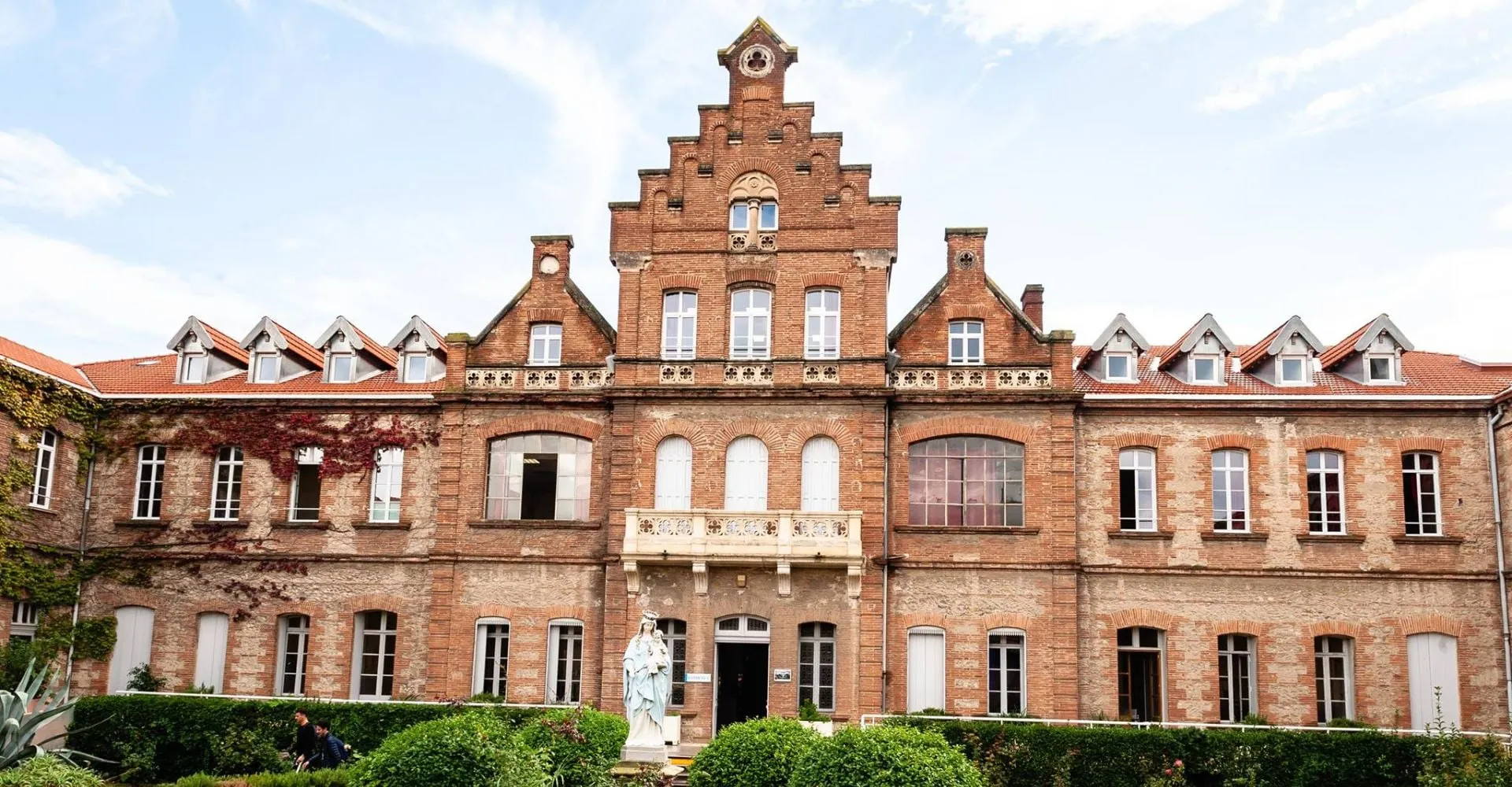 L'edificio del Lycée Notre Dame de Bon Secours, con un caratteristico timpano a gradoni e finestre ad arco, è circondato da un rigoglioso verde.