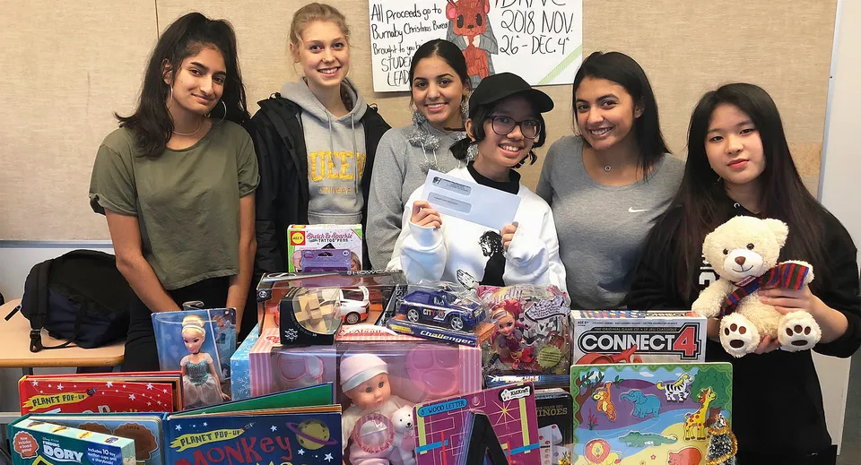 Un gruppo di studentesse sorridenti si trova con giocattoli e regali in un'aula della Cariboo Hill School.