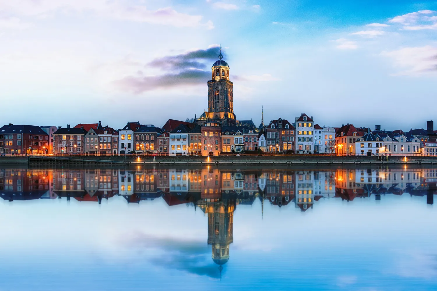 Cittadina olandese sul fiume con torre e case che si riflettono nell'acqua al tramonto