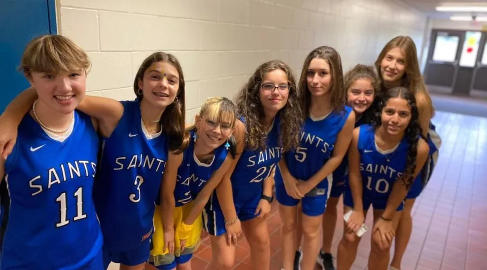 Un gruppo di giovani giocatrici di basket con le divise blu delle Saints nel corridoio della St. Lawrence Secondary School.