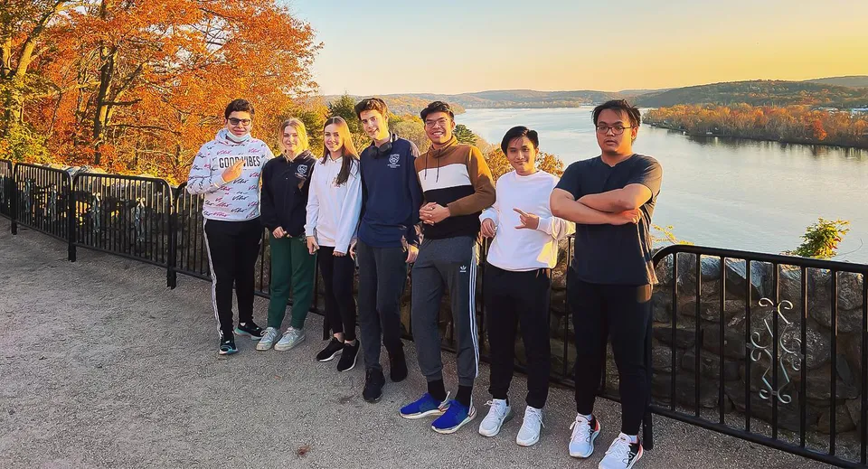 Un gruppo di studenti si trova presso una balaustra con vista sul paesaggio autunnale con lago e montagne vicino alla St. Thomas More School.